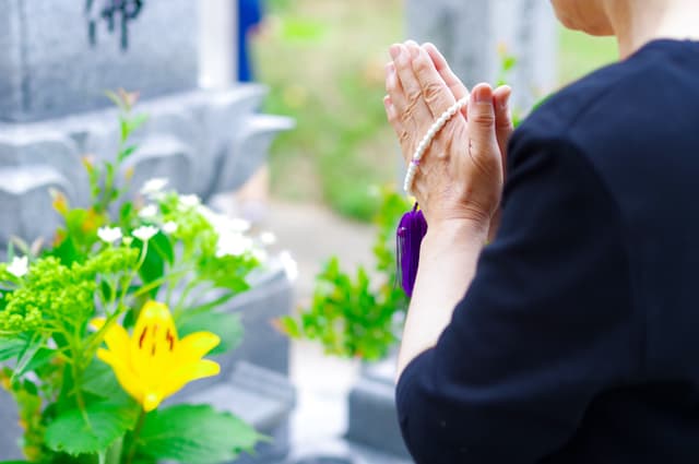 数珠を手にお墓の前で手を合わせる